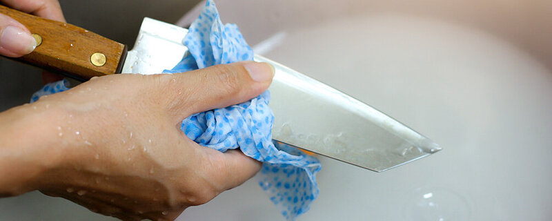 Frau wäscht Küchenmesser sorgfältig ab, da sie damit Geflügel geschnitten hat.