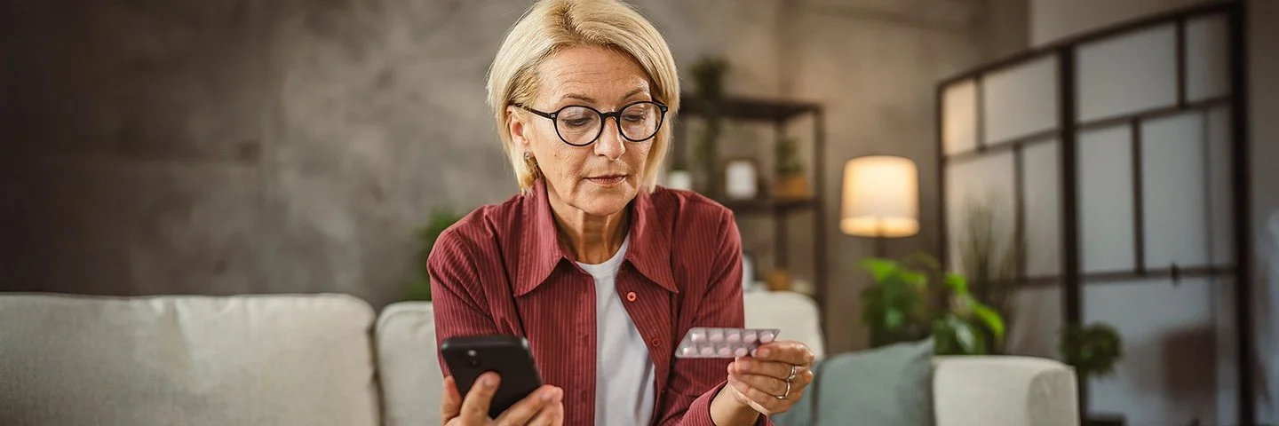 Eine Frau hält in der einen Hand einen Tabletten-Blister und in der anderen ihr Handy.