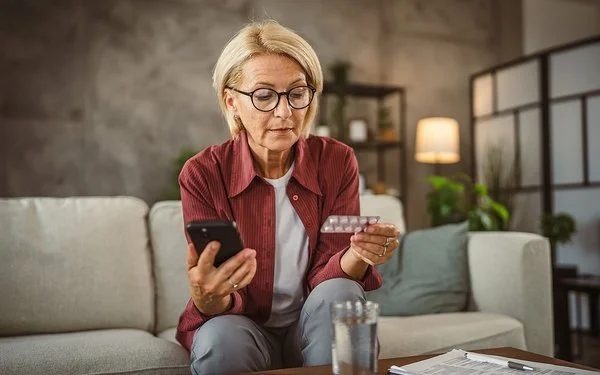 Eine Frau hält in der einen Hand einen Tabletten-Blister und in der anderen ihr Handy.