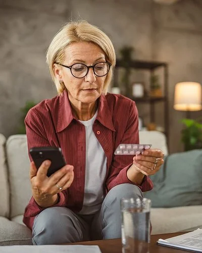 Eine Frau hält in der einen Hand einen Tabletten-Blister und in der anderen ihr Handy.