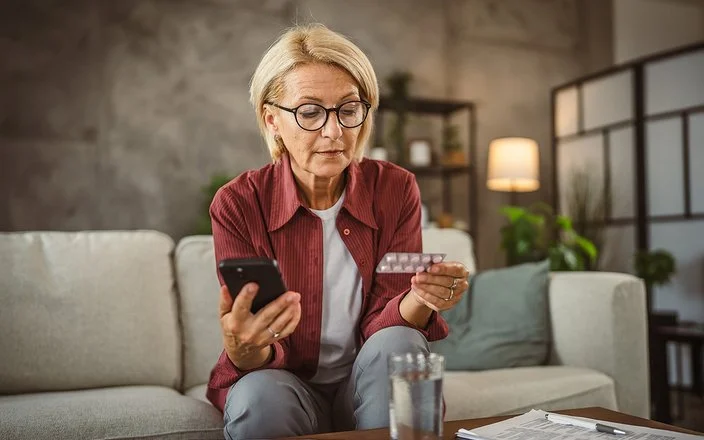 Eine Frau hält in der einen Hand einen Tabletten-Blister und in der anderen ihr Handy.