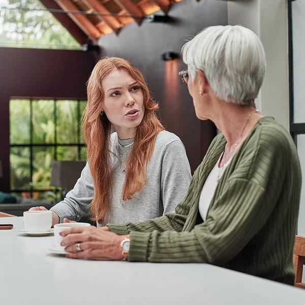 Eine erwachsene Frau spricht mit ihrer Mutter am Esstisch.