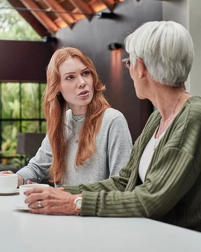 Eine erwachsene Frau spricht mit ihrer Mutter am Esstisch.