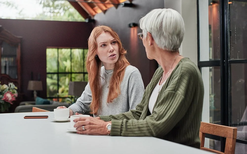 Eine erwachsene Frau spricht mit ihrer Mutter am Esstisch.
