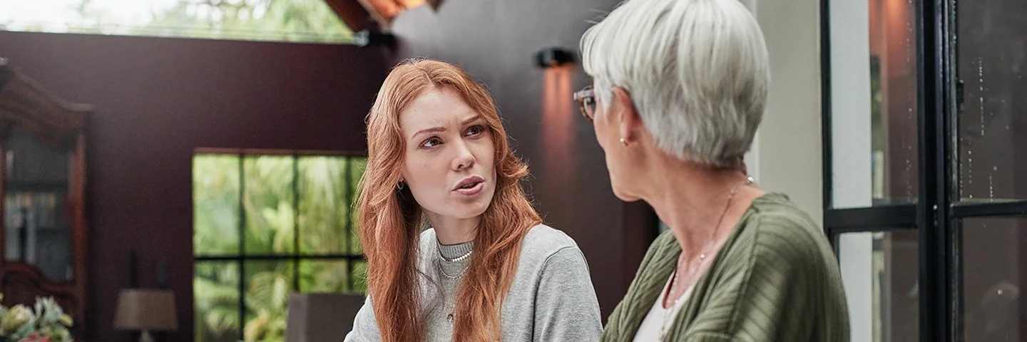 Eine erwachsene Frau spricht mit ihrer Mutter am Esstisch.