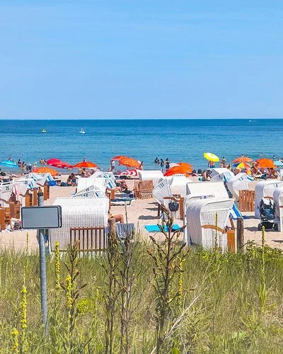 Ein Sandstrand an der Ostsee, der dicht mit Strandkörben und Sonnenschirmen besetzt ist. Die Sonne scheint und das Meer ist ruhig.