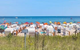 Ein Sandstrand an der Ostsee, der dicht mit Strandkörben und Sonnenschirmen besetzt ist. Die Sonne scheint und das Meer ist ruhig.