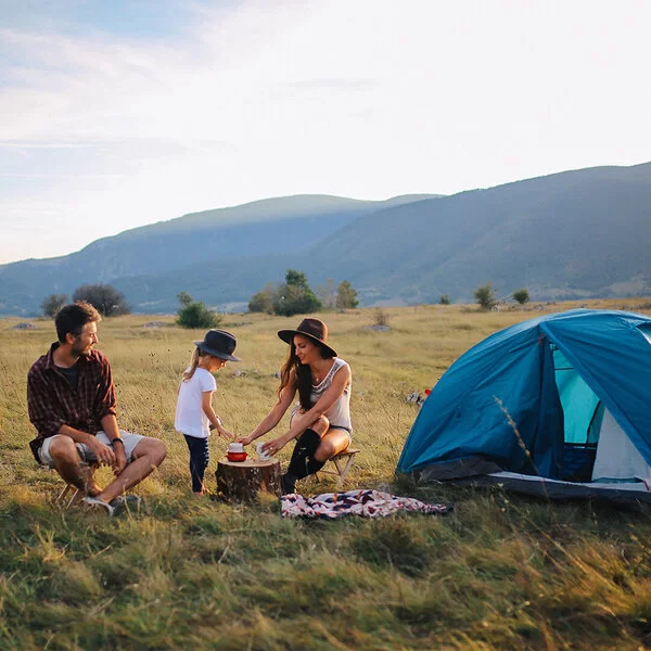 Zwei junge Menschen campen mit einem Kind in der Natur.