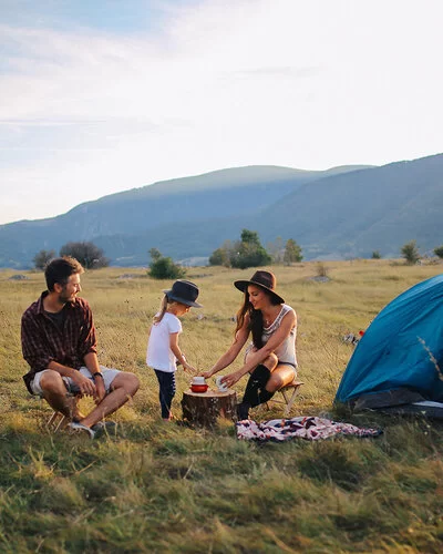 Zwei junge Menschen campen mit einem Kind in der Natur.