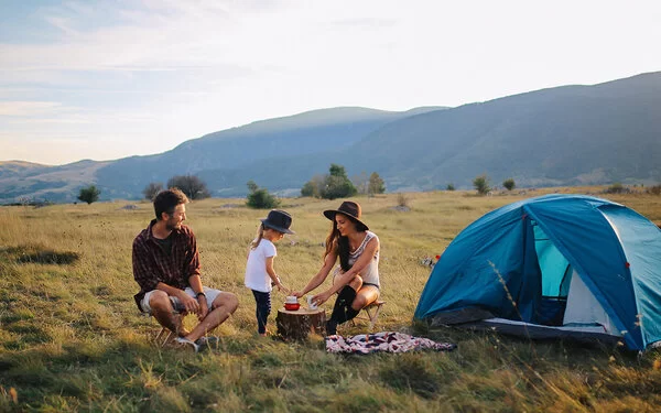 Zwei junge Menschen campen mit einem Kind in der Natur.
