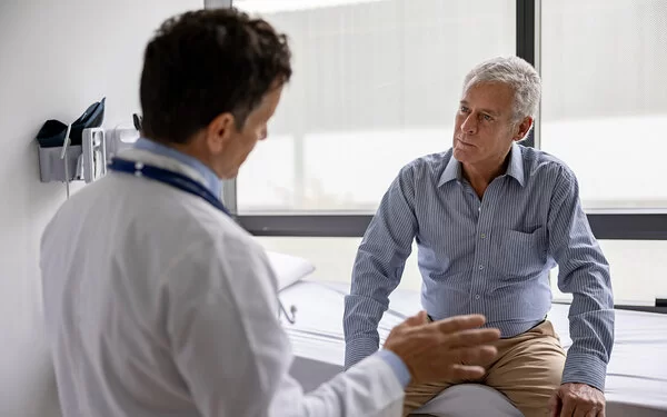 Ein älterer Mann, bei dem der Verdacht auf eine Aortenklappenstenose besteht, bekommt von seinem Kardiologen die nächsten Schritte erklärt.