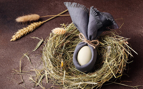 Ein mit einer Stoffserviette umwickeltes Ei liegt in einem selbst gebastelten Osternest aus Stroh.