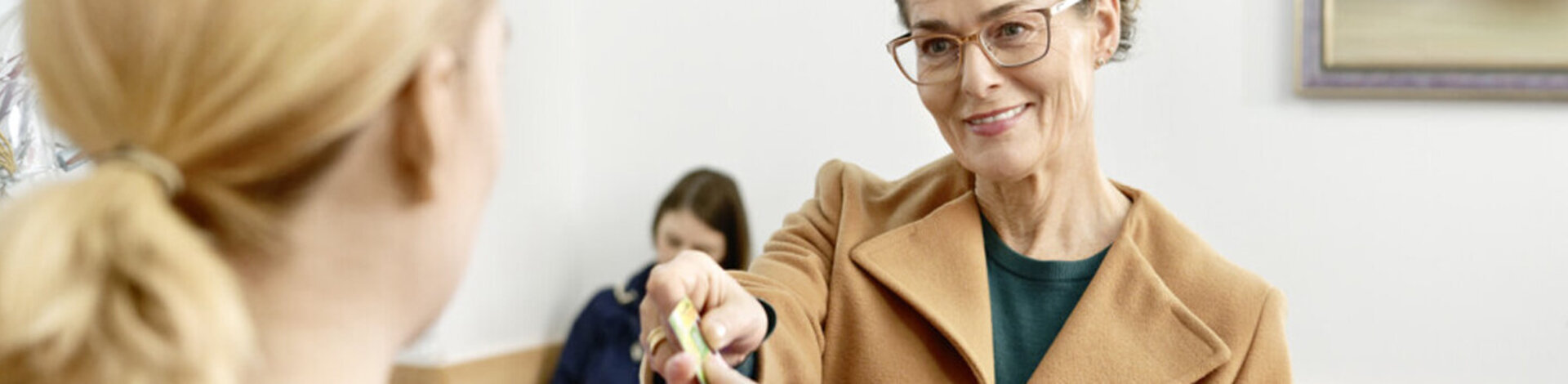 Eine Patientin reicht der Arzthelferin ihre elektronische Gesundheitskarte. Auf dieser sind Daten zur Person und zur Versicherung gespeichert.