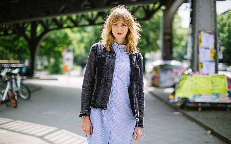 Eine junge Frau, die bei frühlingshaftem Wetter eine Straße in einem urbanen Umfeld entlang läuft.