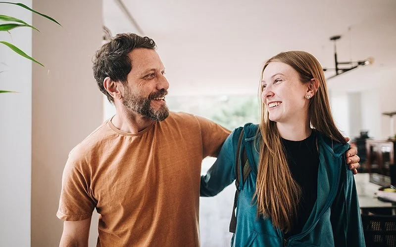Ein Vater und seine Tochter im Teenageralter haben die Arme umeinander gelegt und schauen sich freundlich an.