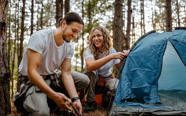 Eine Frau und ein Mann bauen gemeinsam ein Zelt im Wald auf.