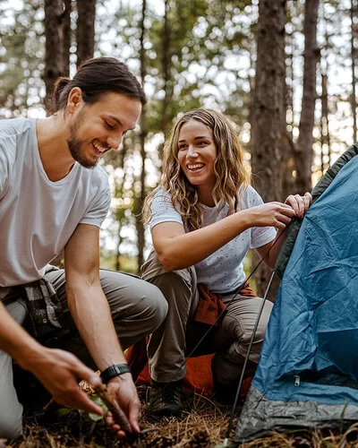 Eine Frau und ein Mann bauen gemeinsam ein Zelt im Wald auf.