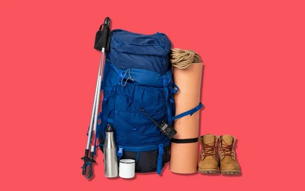 Zwei Wanderstöcke angelehnt an einen Rucksack, daneben stehen eine aufgerollte Matte und zwei Wanderstiefel.