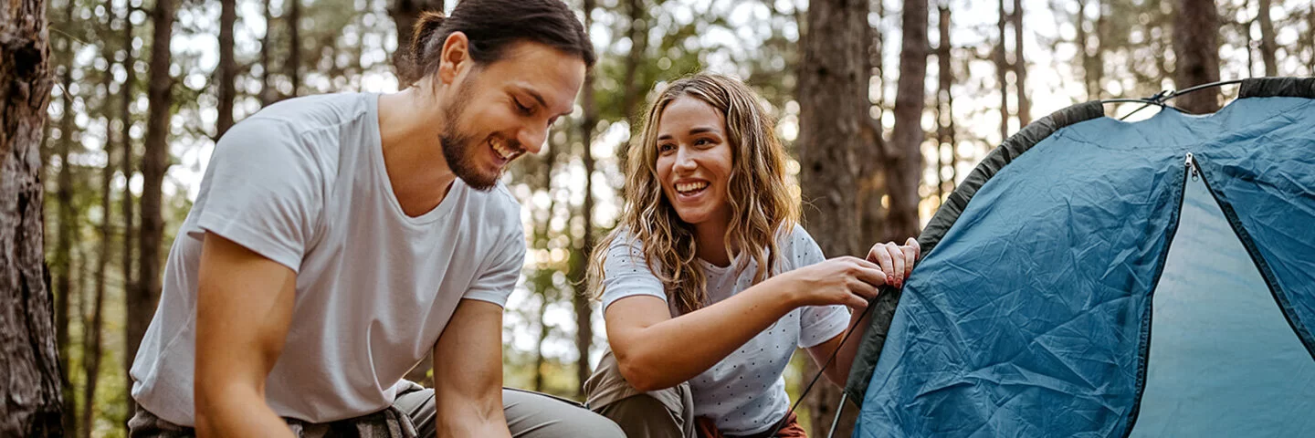 Eine Frau und ein Mann bauen gemeinsam ein Zelt im Wald auf.