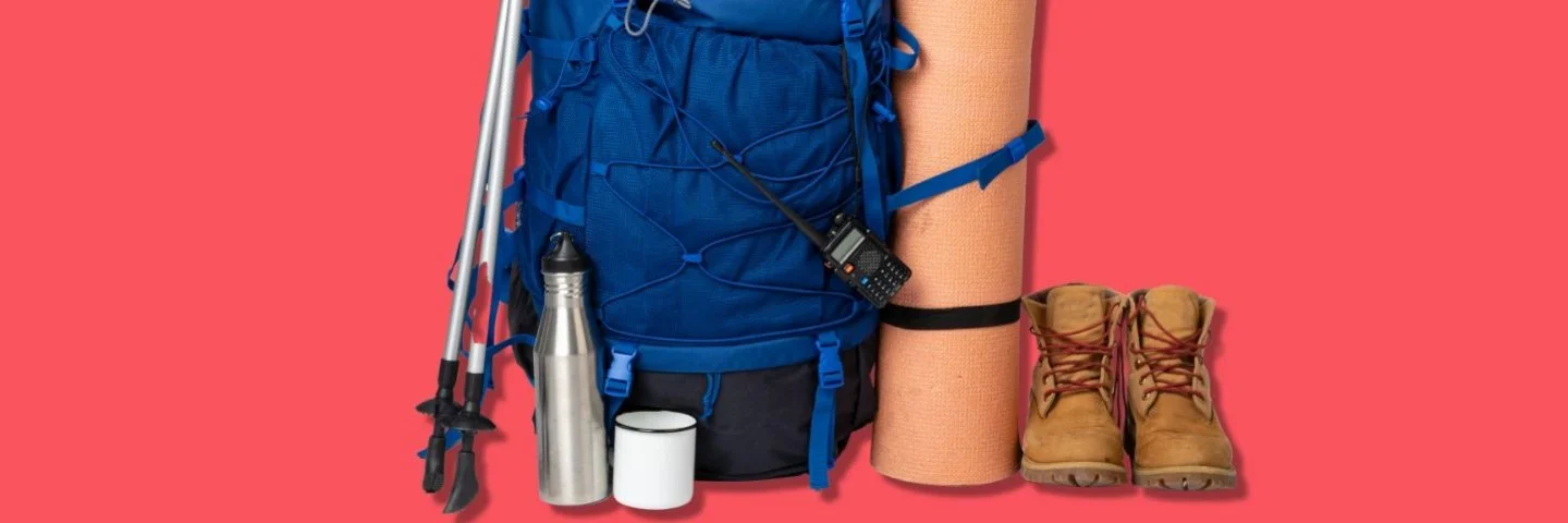 Zwei Wanderstöcke angelehnt an einen Rucksack, daneben stehen eine aufgerollte Matte und zwei Wanderstiefel.