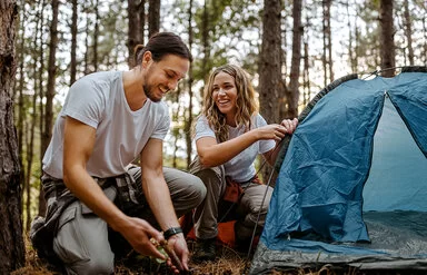 Eine Frau und ein Mann bauen gemeinsam ein Zelt im Wald auf.