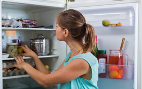 Eine junge Frau räumt Lebensmittel in einen Kühlschrank ein.