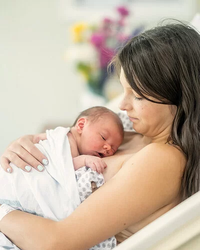 Eine junge Mutter liegt auf einer Geburtsstation im Bett. Ihr Neugeborenes liegt auf ihrer Brust.