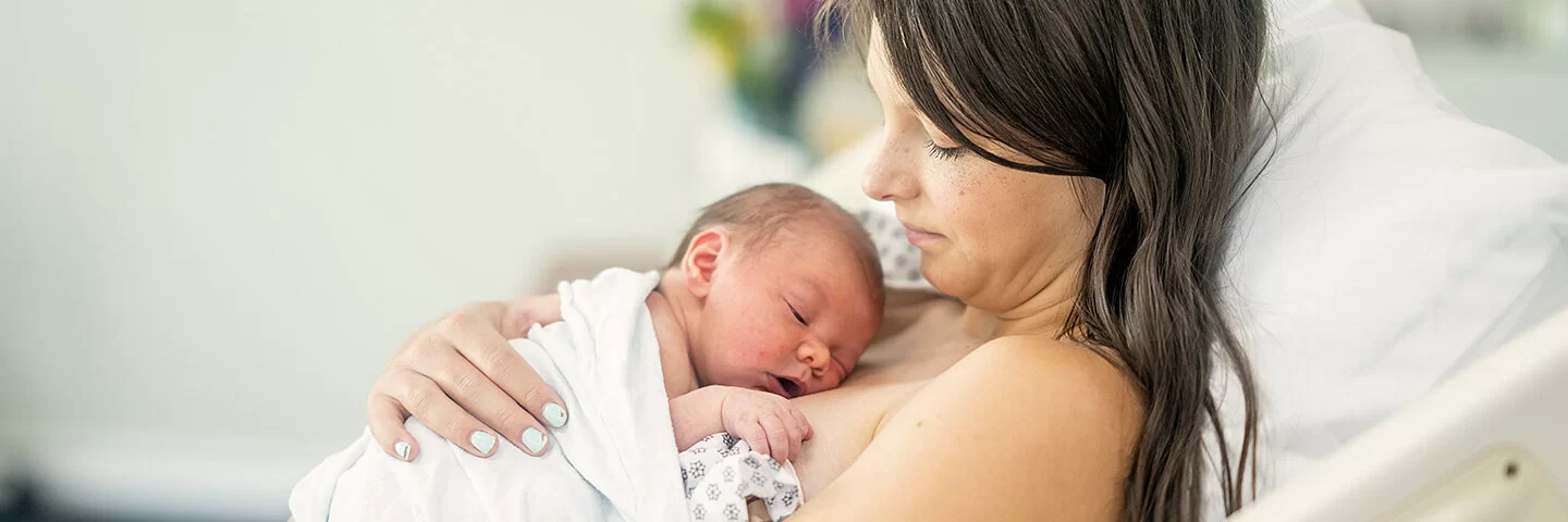Eine junge Mutter liegt auf einer Geburtsstation im Bett. Ihr Neugeborenes liegt auf ihrer Brust.