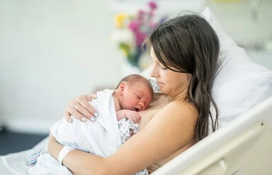 Eine junge Mutter liegt auf einer Geburtsstation im Bett. Ihr Neugeborenes liegt auf ihrer Brust.