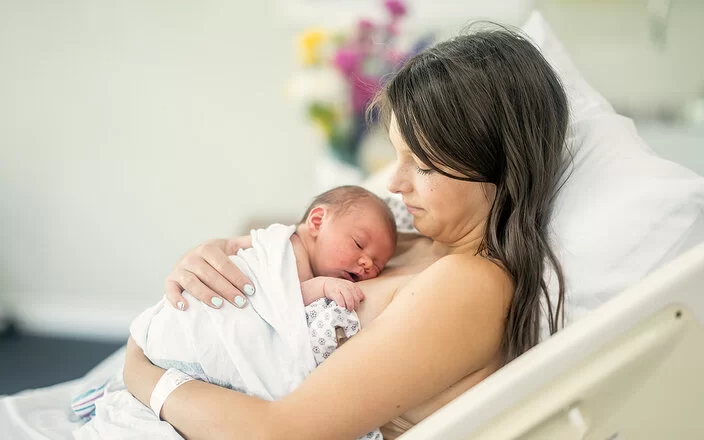 Eine junge Mutter liegt auf einer Geburtsstation im Bett. Ihr Neugeborenes liegt auf ihrer Brust.