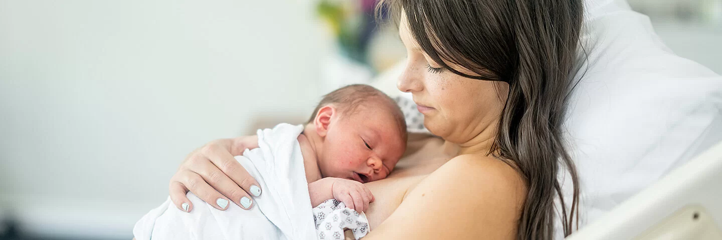 Eine junge Mutter liegt auf einer Geburtsstation im Bett. Ihr Neugeborenes liegt auf ihrer Brust.