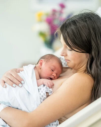 Eine junge Mutter liegt auf einer Geburtsstation im Bett. Ihr Neugeborenes liegt auf ihrer Brust.