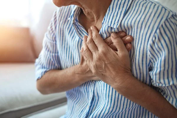 Eine Frau drückt beide ihrer Hände an ihre Brust.