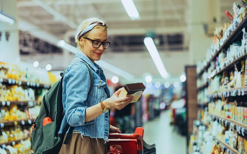 Eine Frau mit einem Stirnband liest sich im Supermarkt eine Produktbeschreibung durch.