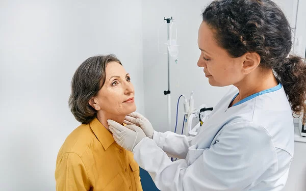 Ältere Frau leidet an Hashimoto-Thyreoiditis und lässt ihre Schilddrüse von einer Ärztin untersuchen.