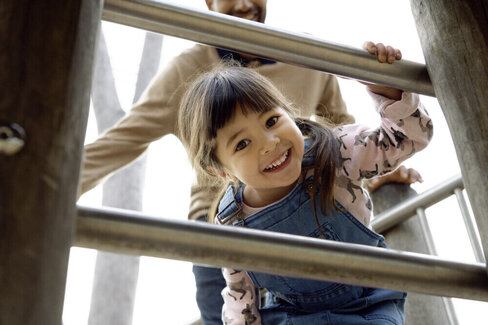 Ein Mädchen auf einem Klettergerüst. Ein Erwachsener steht hinter ihr. Mit der AOK Kinder-Krankenzusatzversicherung sind Kinder bestens abgesichert.