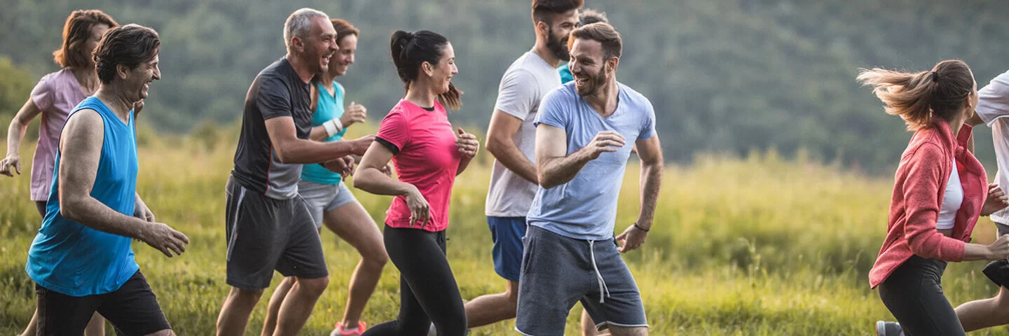 Eine Gruppe Menschen gemischten Alters joggt durch die Natur und lacht gemeinsam.