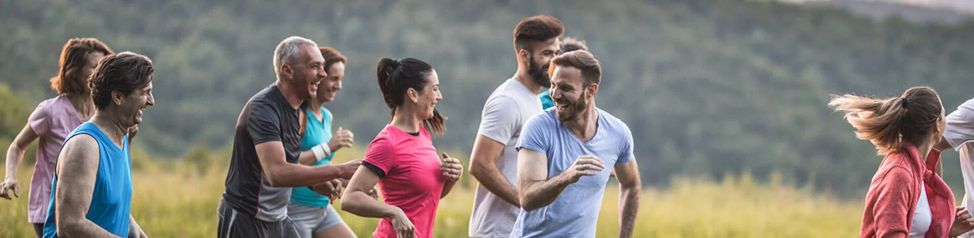 Eine Gruppe Menschen gemischten Alters joggt durch die Natur und lacht gemeinsam.