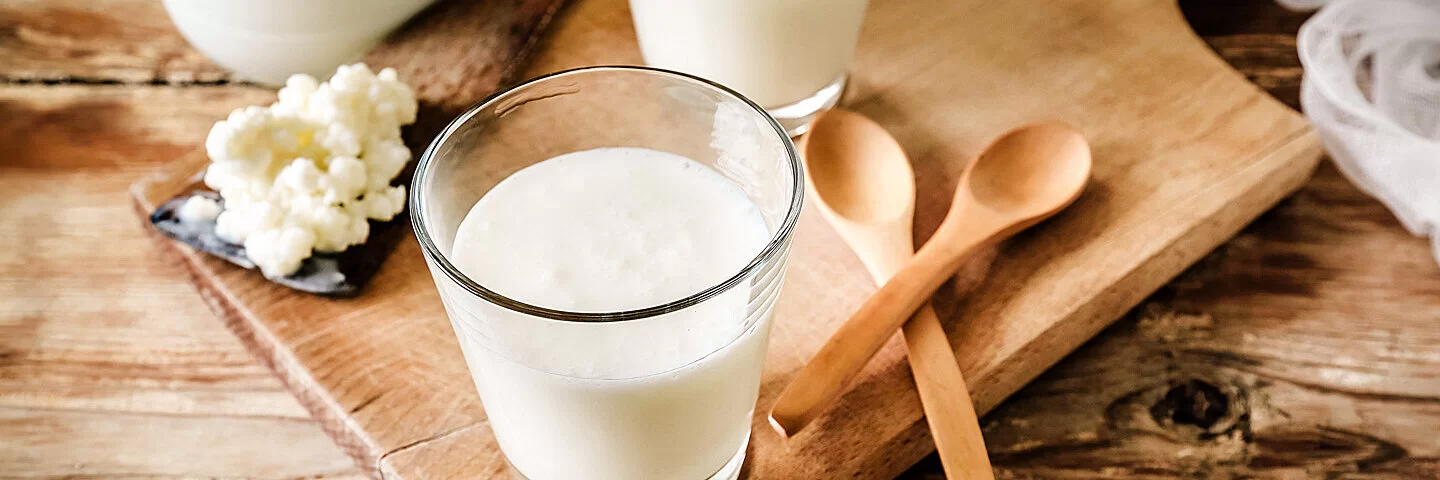 Zwei Gläser mit Kefir, der Probiotika enthält, sind auf einem Holzbrett angerichtet.