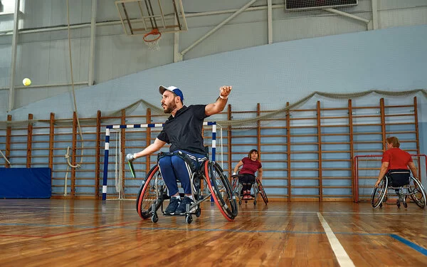 Mann im Rollstuhl spielt Tennis in einer Turnhalle.