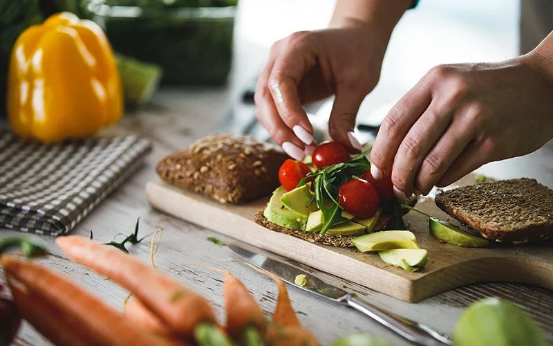Eine Frau belegt ein Vollkornbrot mit frischen Zutaten.