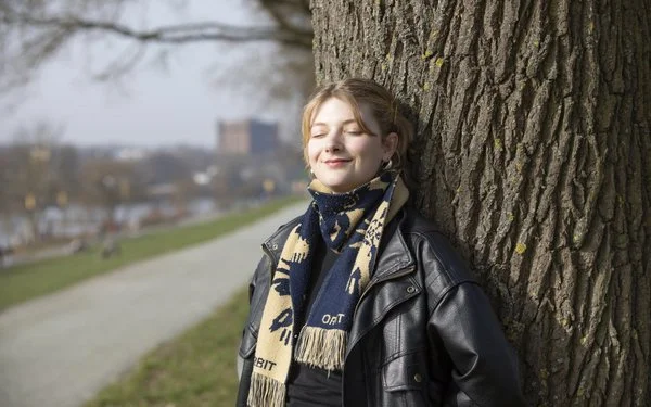 Liz Rusche lehnt in der Sonne an einem Baum. Sie lächelt und hat die Augen geschlossen.