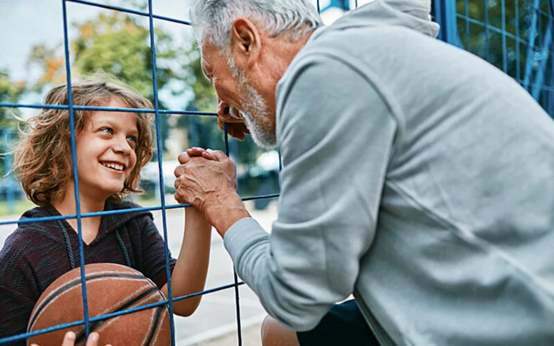 Ein Großvater und Enkel spielen zusammen Basketball und schlagen sich durch einen Zaun in die Hände ein.