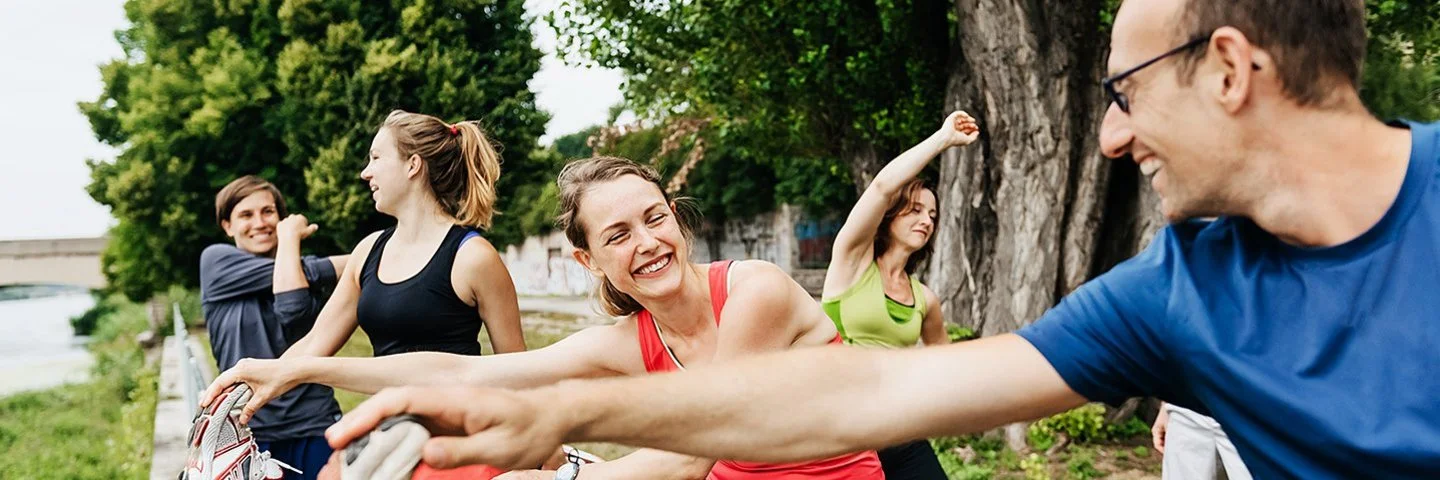 Ein Gruppe von Menschen in Sportkleidung macht in der Natur Dehnübungen.