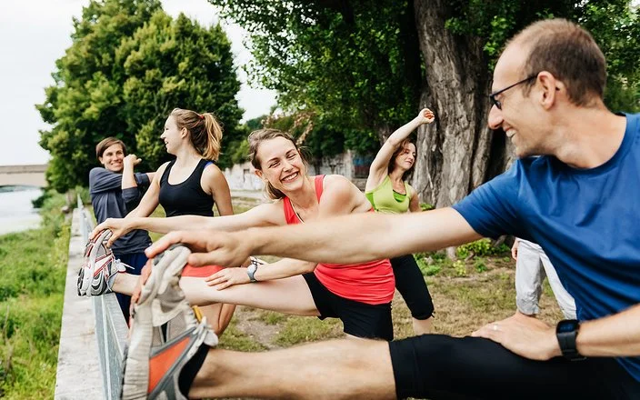 Ein Gruppe von Menschen in Sportkleidung macht in der Natur Dehnübungen.