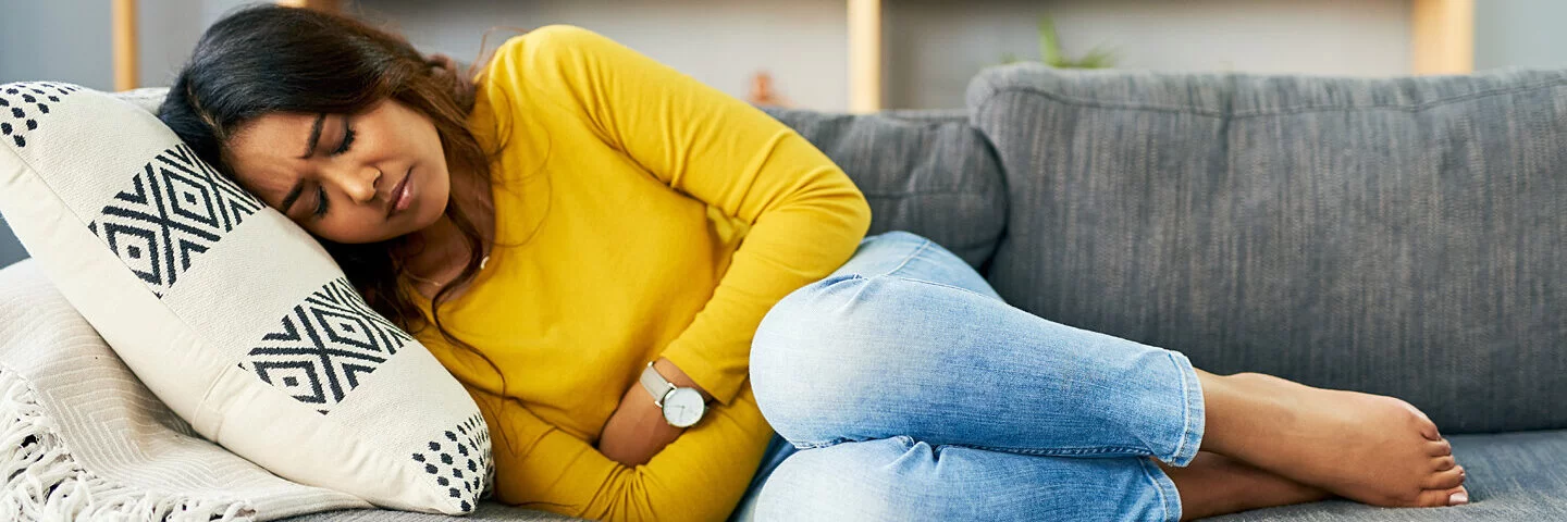 Eine Frau mit Myomen und Krämpfen liegt auf der Couch und hält sich den Unterleib.