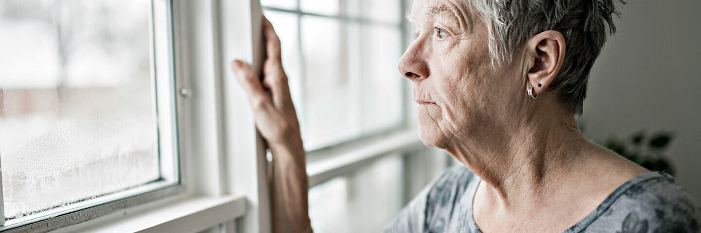 Frau, die an Altersschwäche leidet, guckt aus dem Fenster und hat den Lebensmut verloren.