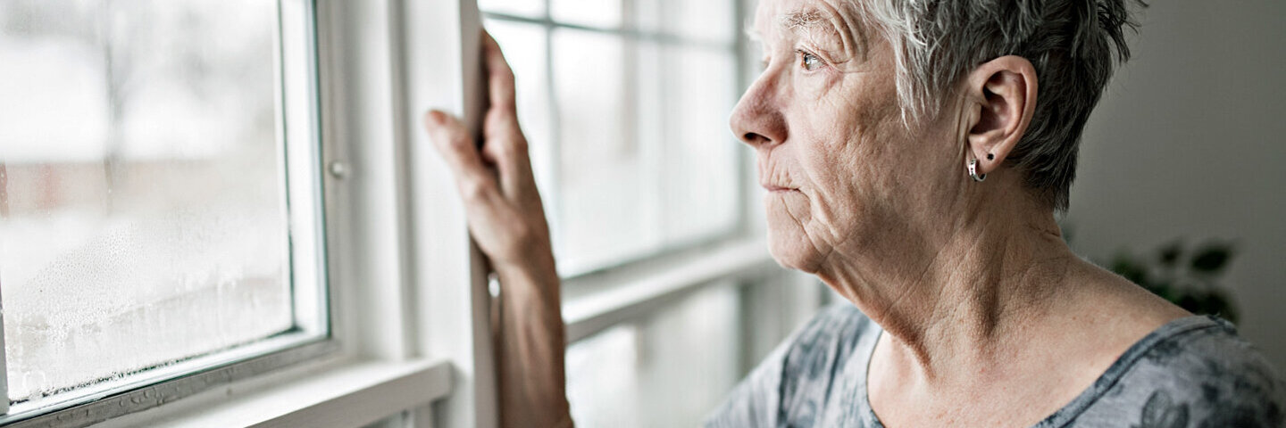 Frau, die an Altersschwäche leidet, guckt aus dem Fenster und hat den Lebensmut verloren.