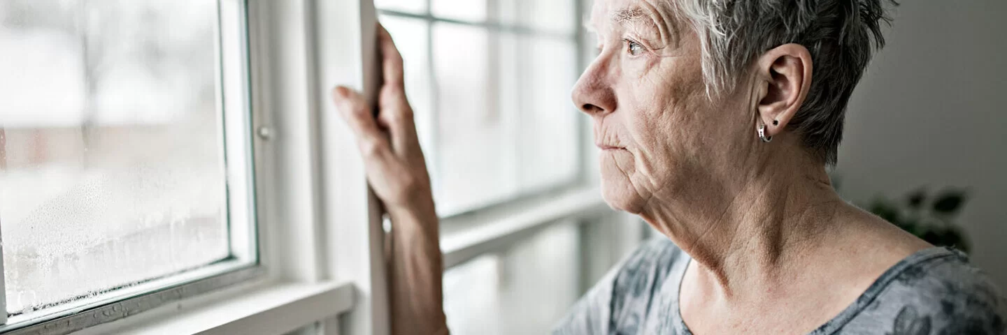 Frau, die an Altersschwäche leidet, guckt aus dem Fenster und hat den Lebensmut verloren.