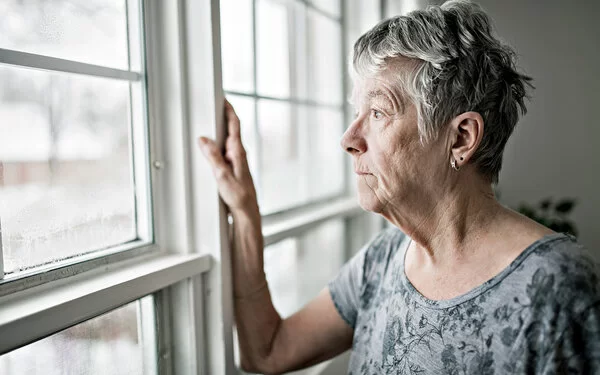 Frau, die an Altersschwäche leidet, guckt aus dem Fenster und hat den Lebensmut verloren.